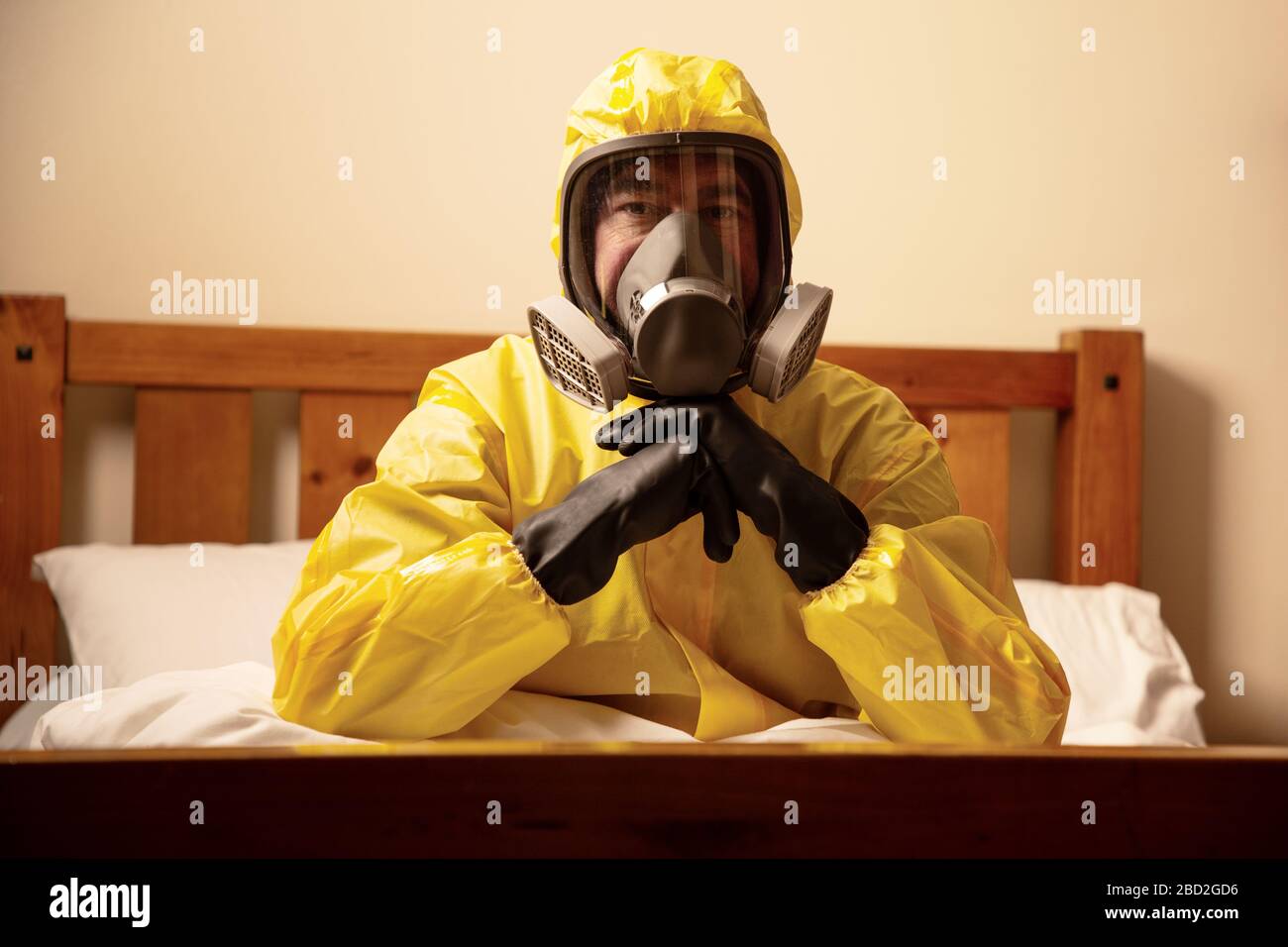 Mann selbstisolierend im Bett mit einem Hazmatanzug und einer Maske Stockfoto