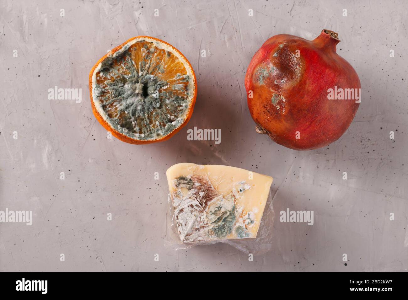 Verdorbene faule Speisen mit Schimmel: Halbe Orange, Granatapfel und Hartkäse auf grauem Hintergrund, Draufsicht Stockfoto