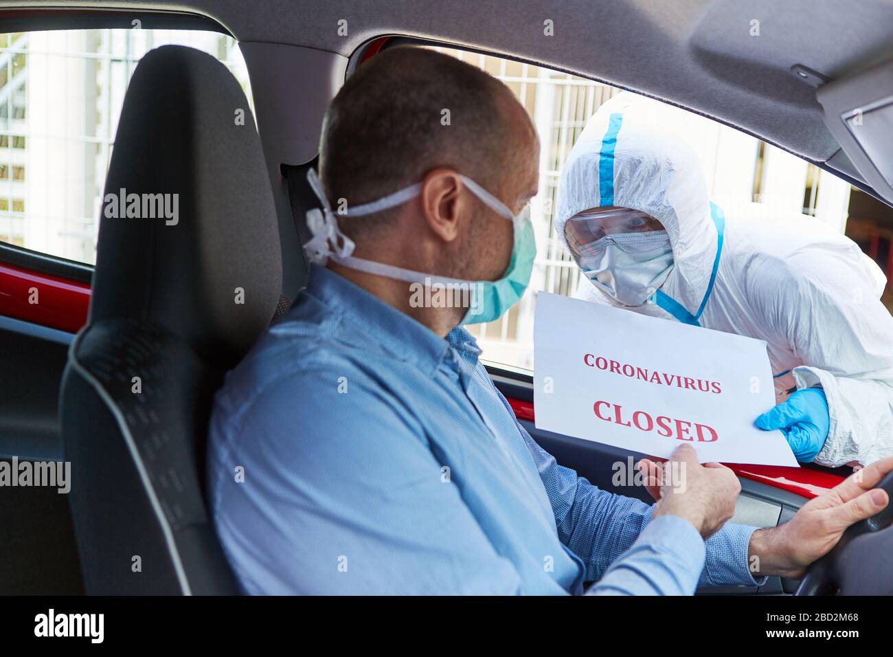 Autofahrer mit Gesichtsmasken werden von Mitarbeitern in Schutzkleidung über Verschlüsse von Coronavirus informiert Stockfoto