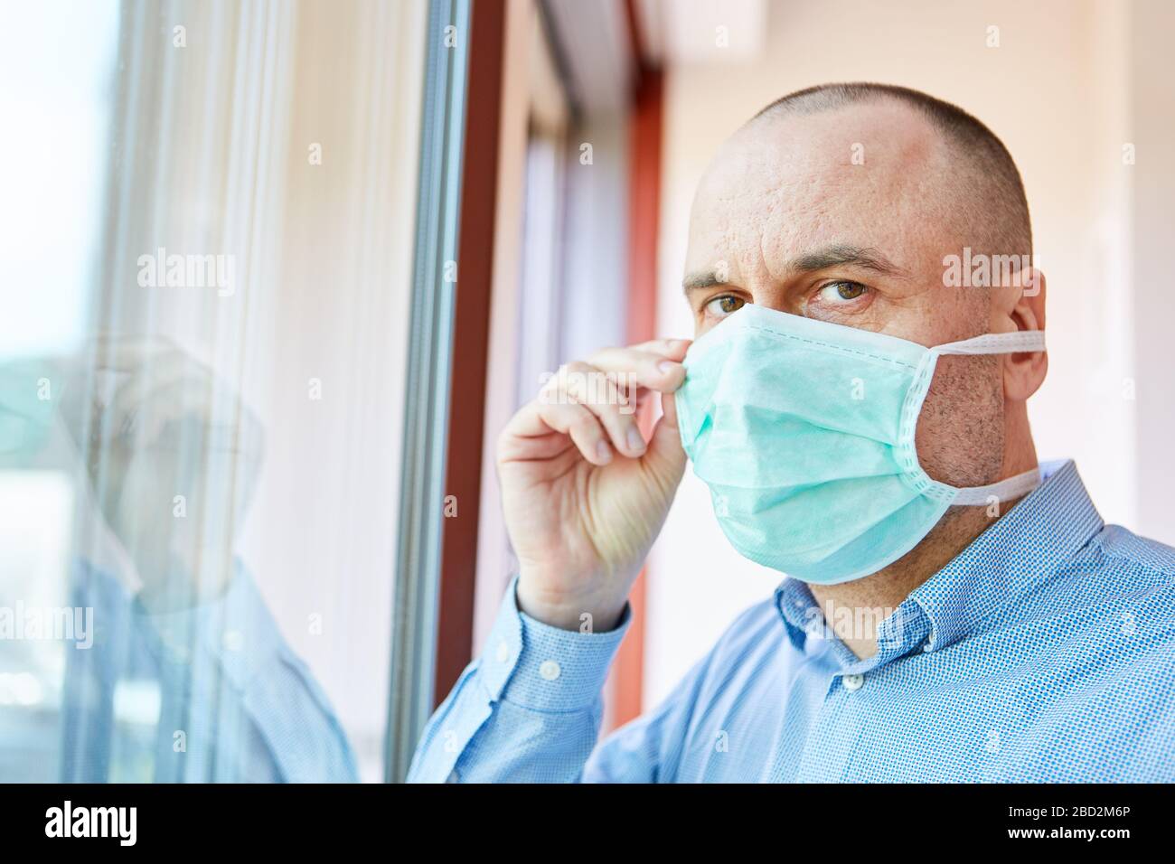 Senior als Covid-19-Patient mit Mundschutz zu Hause unter Quarantäne bei einer Coronavirus-Epidemie Stockfoto