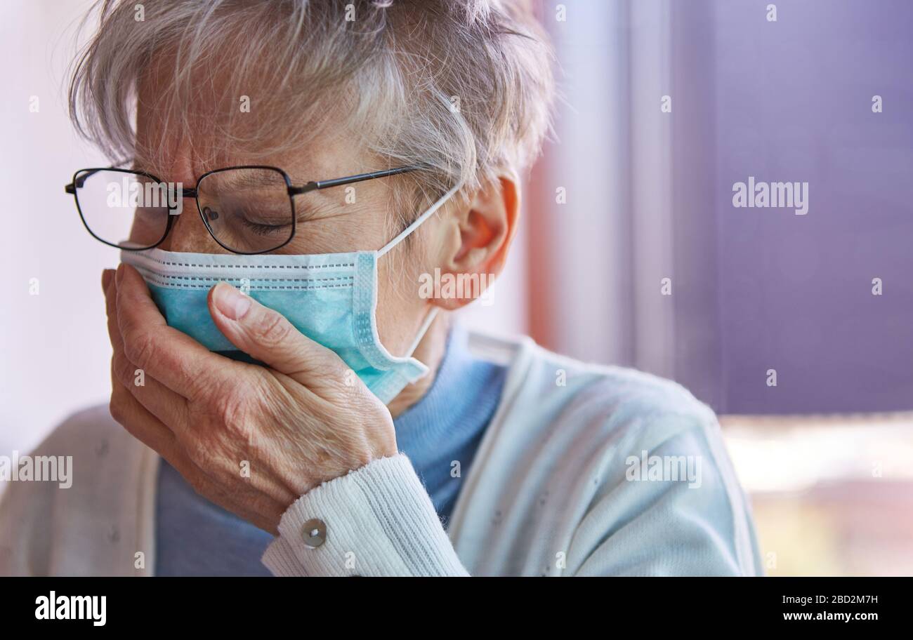Seniorin mit Quarantäne-Gesichtsmaske hustet während einer Coronavirus-Pandemie in der Hand Stockfoto