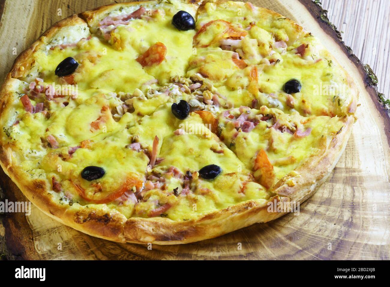 Pizza in Scheiben mit Wurst, Speck, Oliven und Tomaten ist auf einem Holztisch. Fast Food Stockfoto