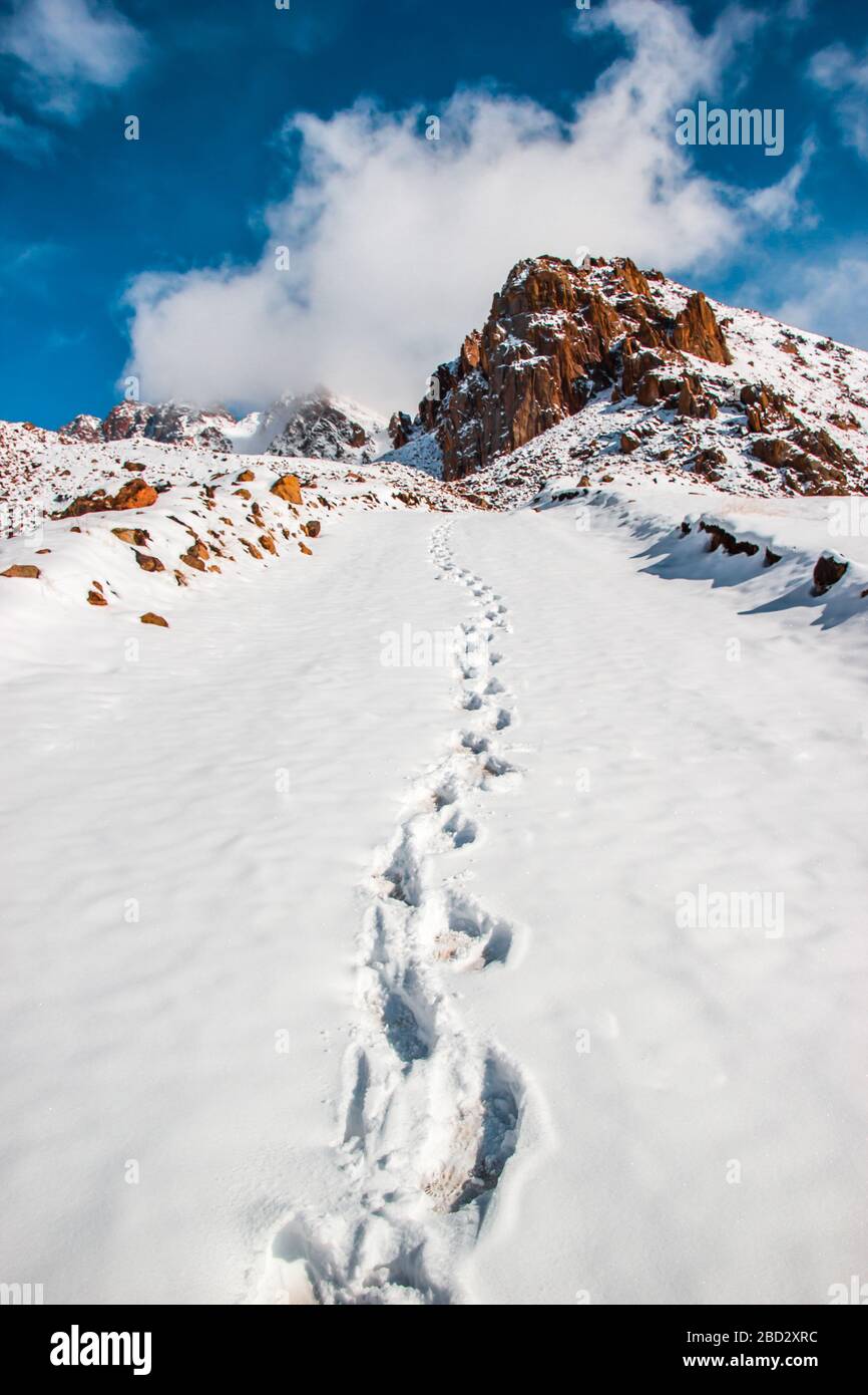 Tiefe Spuren im weißen Schnee. Schneedecke und Wolken inmitten des blauen Himmels. Winter Mountain Travel Konzept Stockfoto