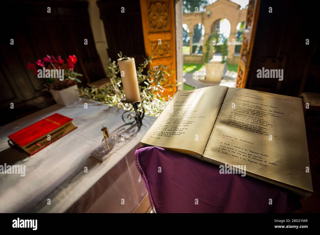 Weitwinkelansicht einer für die Messe geschmückten Kapelle, mit einer heiligen bibel im Vordergrund und einer Tür, die zu einem Garten hin offen ist Stockfoto