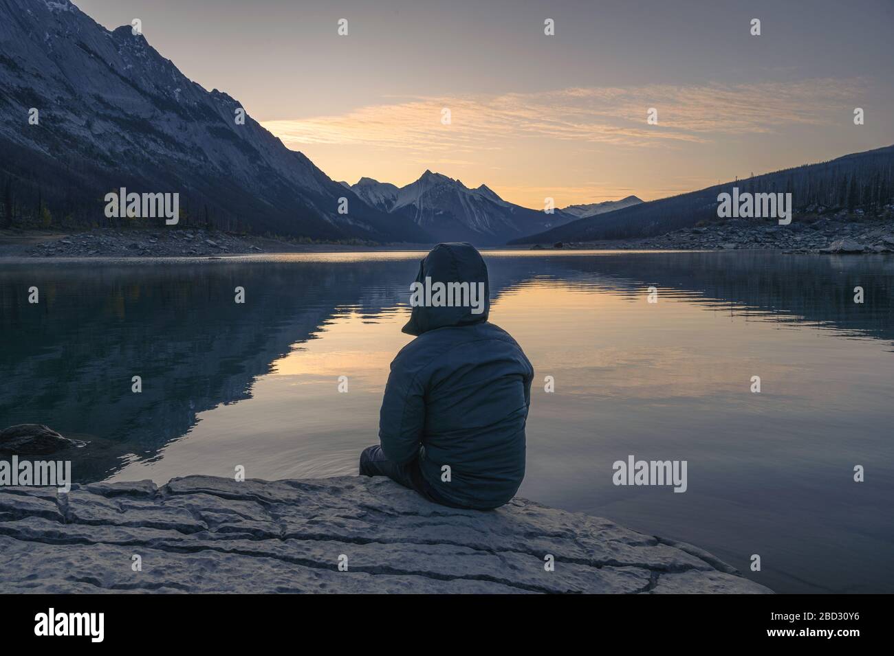 Man Traveler sitzt am Morgen auf dem Felsen im Medicine Lake im Jasper Nationalpark, Kanada Stockfoto