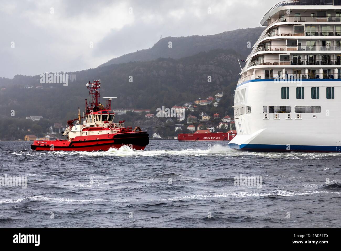 Schleppboot BB Coaster unterstützt ein großes Kreuzfahrtschiff bei der Abfahrt vom Hafen von Bergen, Norwegen. Ein regnerischer und nebeliger Tag Stockfoto