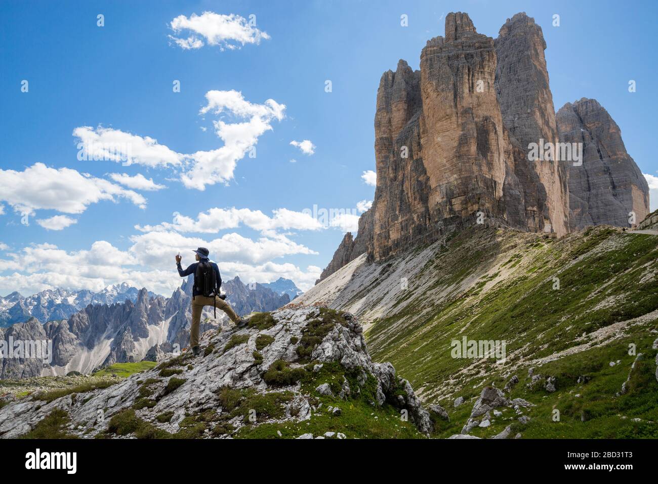 Weitwinkelansicht einer sommerlichen Berglandschaft, mit einem Wanderer, der sich im Vordergrund selbst macht, und den drei Gipfeln des Lavaredo im Hintergrund Stockfoto