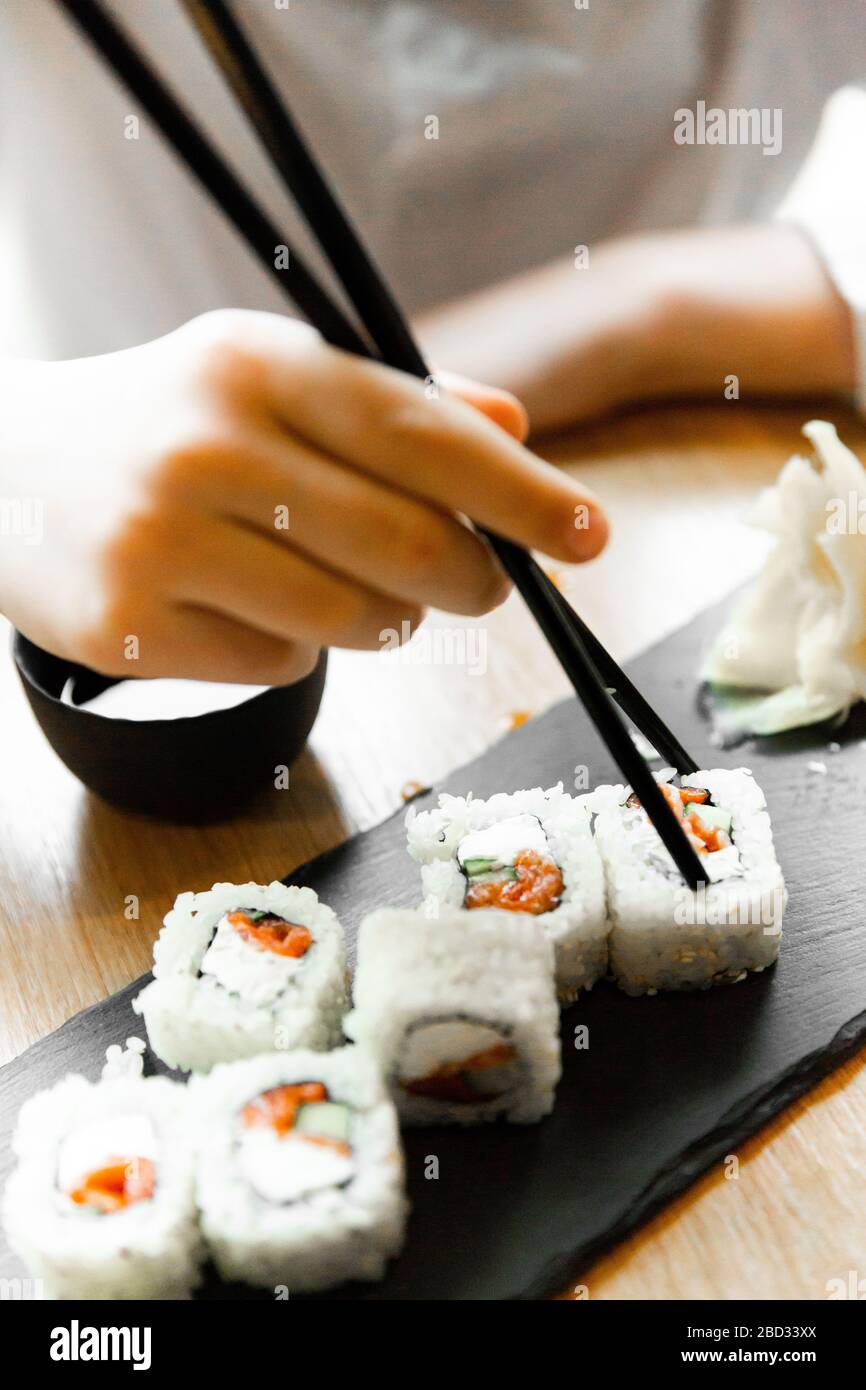 Mann, der einen Essstäbchen mit Lachenrolle auf dem Restauranttisch hält. Asiatischer Mann, der Lachsrollen im asiatischen Restaurant isst. Stockfoto