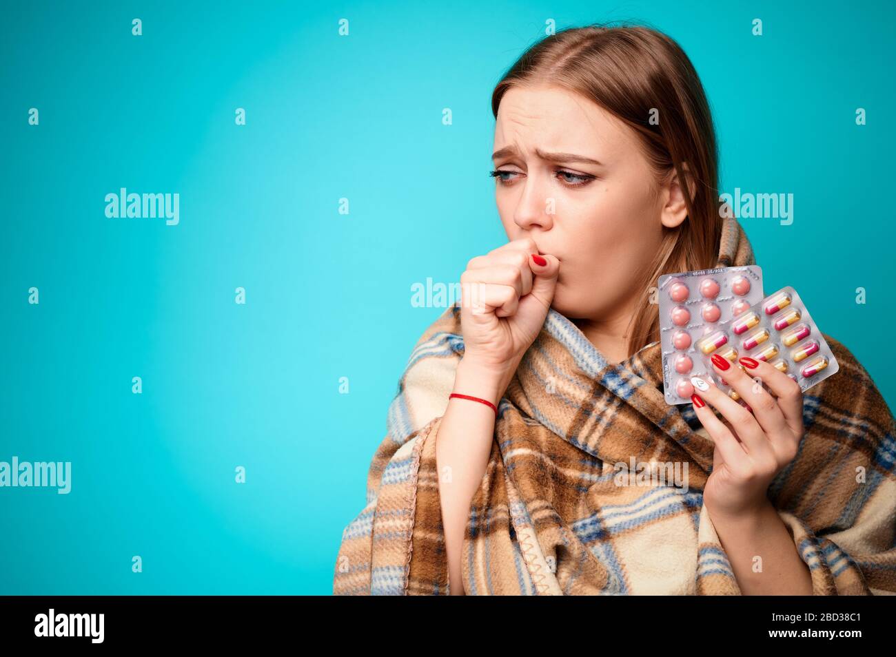Frau mit einem Virus hustet und hält Pillen in ihren Händen, die in eine Pflauge eingewickelt sind. Blauer Hintergrund Stockfoto