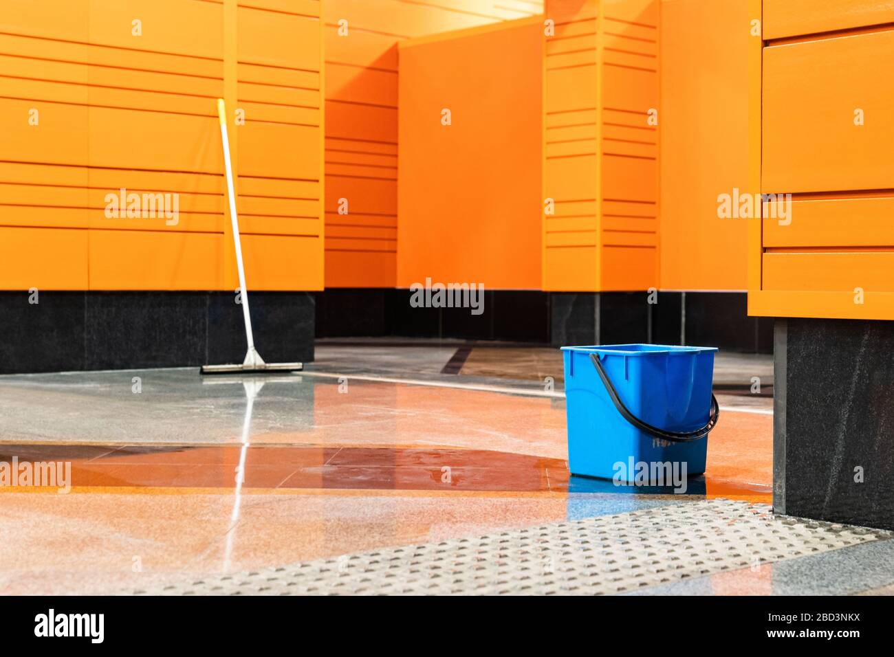 Desinfektion von U-Bahn-Stationen während der Coronavirus-Pandemie. Blauer Plastikbecher und Mopp vor dem Hintergrund einer leeren Station mit orangefarbenem wa Stockfoto