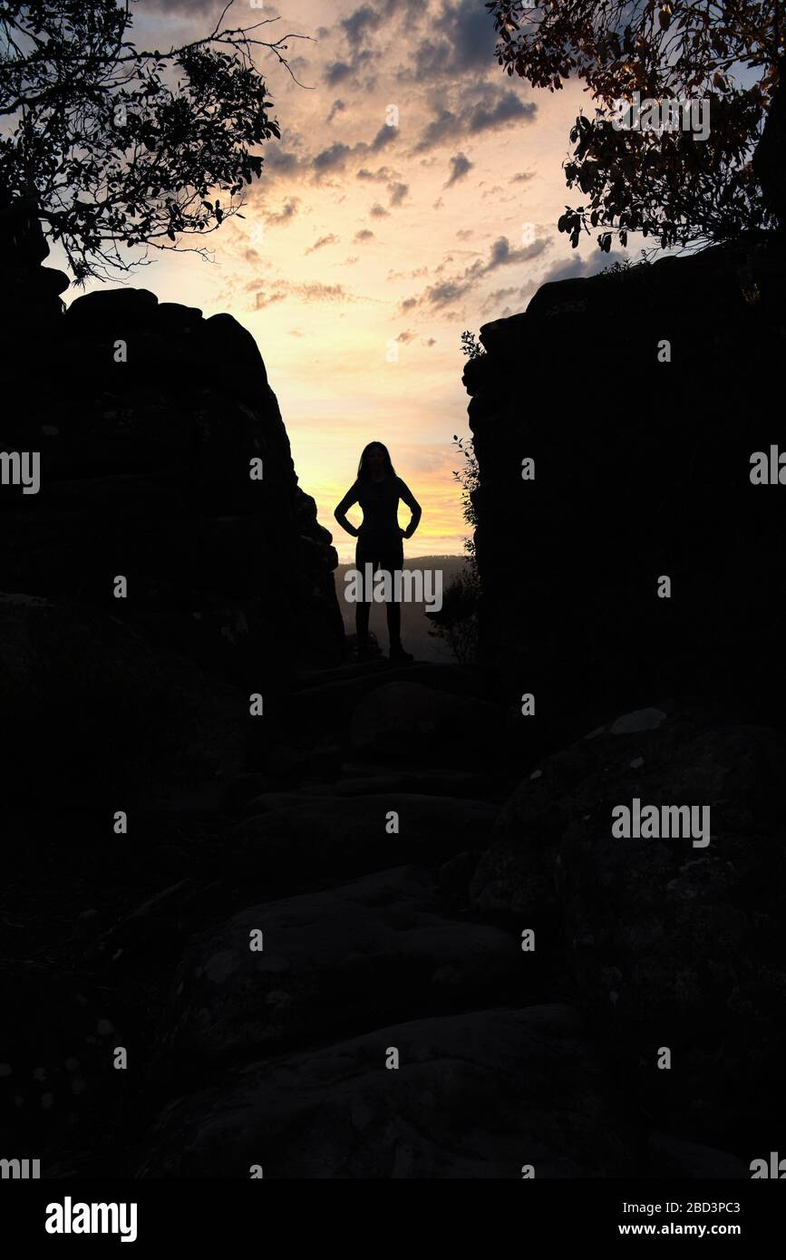 Silhouetten-Abenteuerreisende stehen in einer Lücke zwischen zwei Felsblöcken bei einem Aussichtspunkt auf dem Pinnacle Track Walk in den Grampians in Victoria. Stockfoto