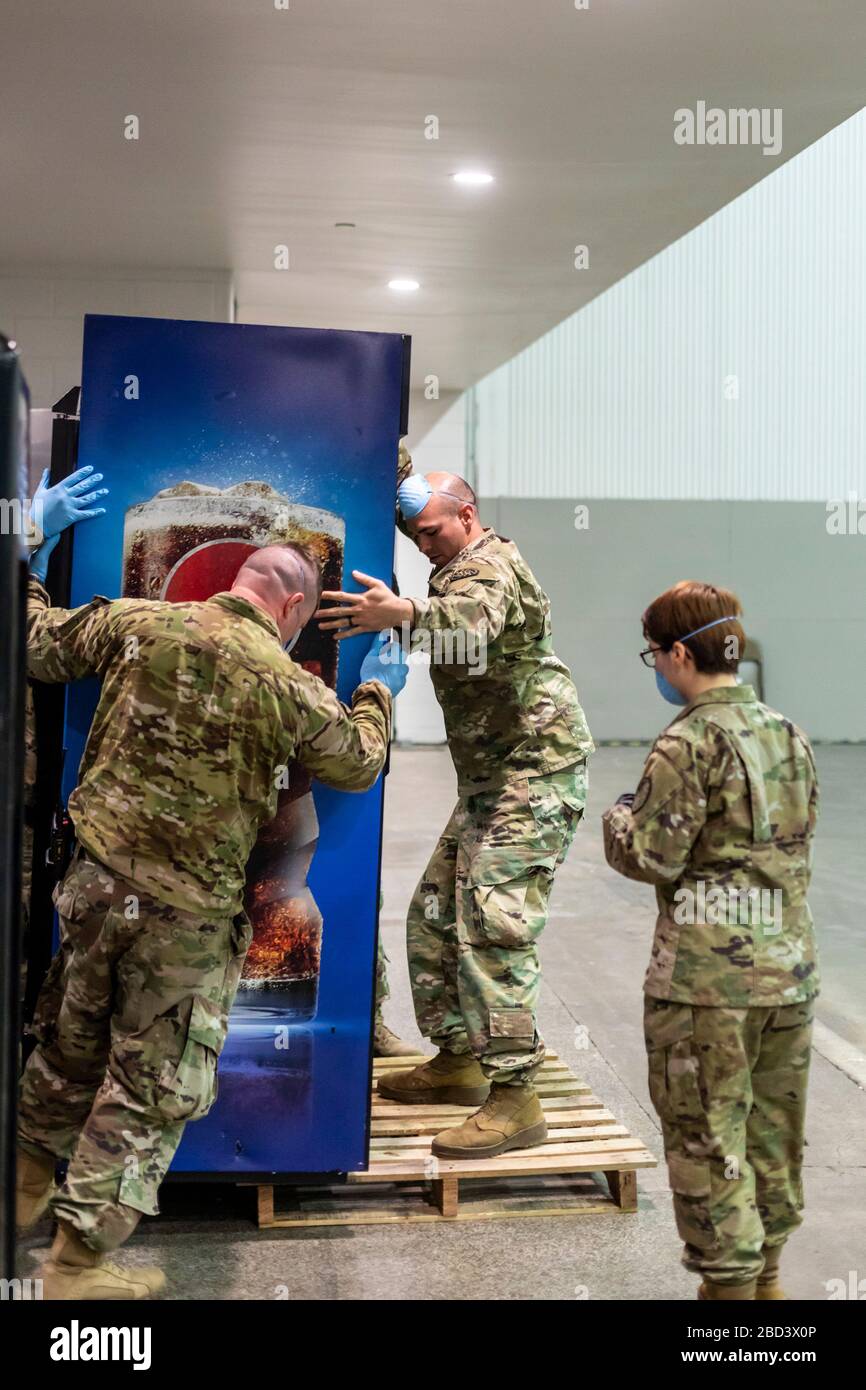 Detroit, Michigan, USA. April 2020. Arbeiter bauen ein Notarztkrankenhaus im TCF-Kongresszentrum auf. Das Krankenhaus mit 1.000 Betten wird Covid-19-Patienten versorgen. Mitglieder der Michigan National Guard bewegen einen Getränkekühler. Kredit: Jim West/Alamy Live News Stockfoto