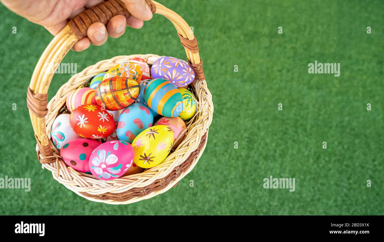 Nahaufnahme der Hand, die bunte ostereier im Korb über grünem Grasboden trägt. Stockfoto