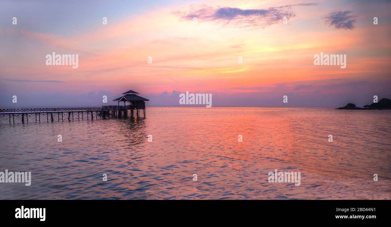 Panorama eines romantischen Sonnenuntergangs der goldenen tropischen Lagune auf der Insel Bintan in Indonesien mit Silhouette einer Jetthütte. Stockfoto