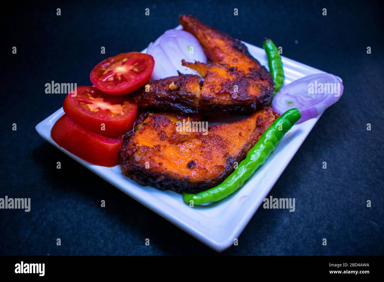 Frittierter Fisch in weißem Teller mit Green Chili, Onion und Tomato auf schwarzem Hintergrund Stockfoto