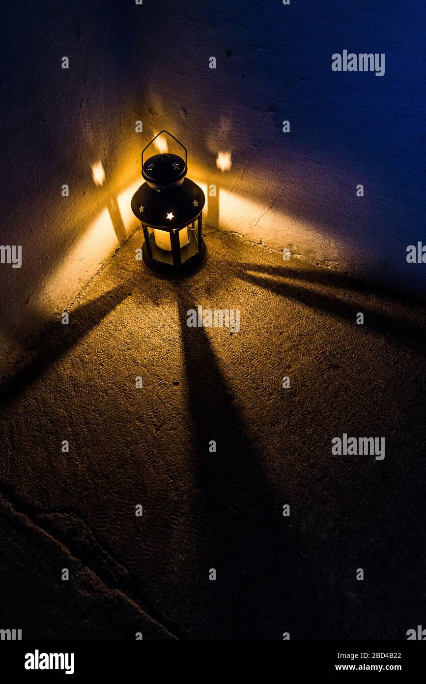 Symmetrische Weitwinkel-Nachtaufnahme einer Kerze angezündeten Laterne Langgestreckte Schatten auf die raue Oberfläche des Bodens werfen Stockfoto