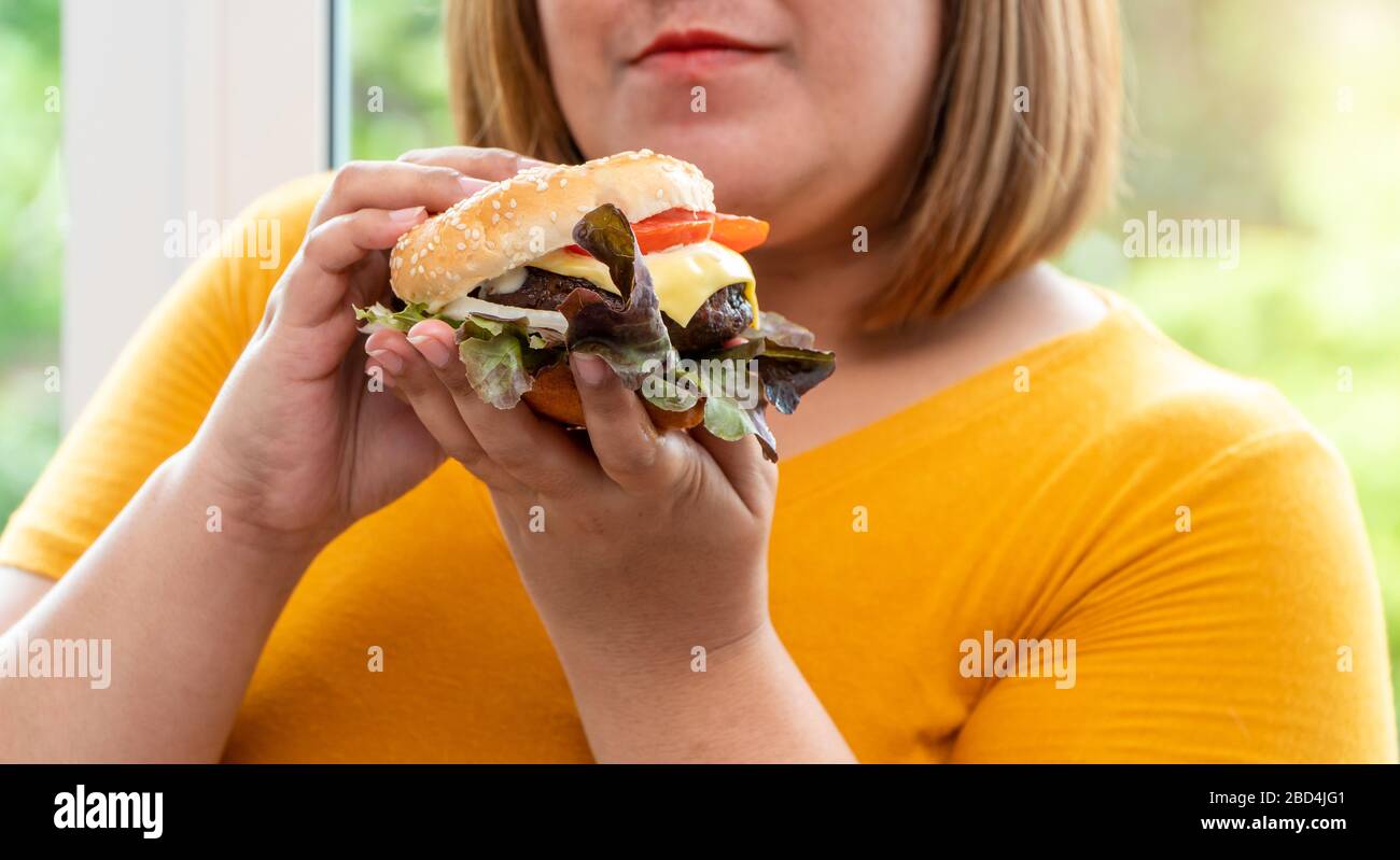 Hungrige, übergewichtige junge asiatin, die Hamburger hält, ihre hungrigen und überernährten, gluttonigen und bingen Essen. Ihr Lebensstil isst fast Food a Stockfoto