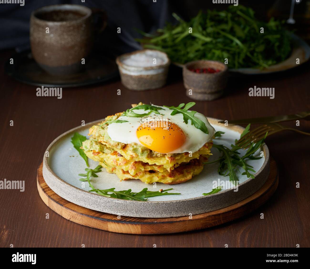 KartoffelWaffeln mit frittiertem Ei, Arugula und Avocado-Sauce. Herzhaftes fettes Frühstück. Dunkelbrauner Tisch. Stockfoto