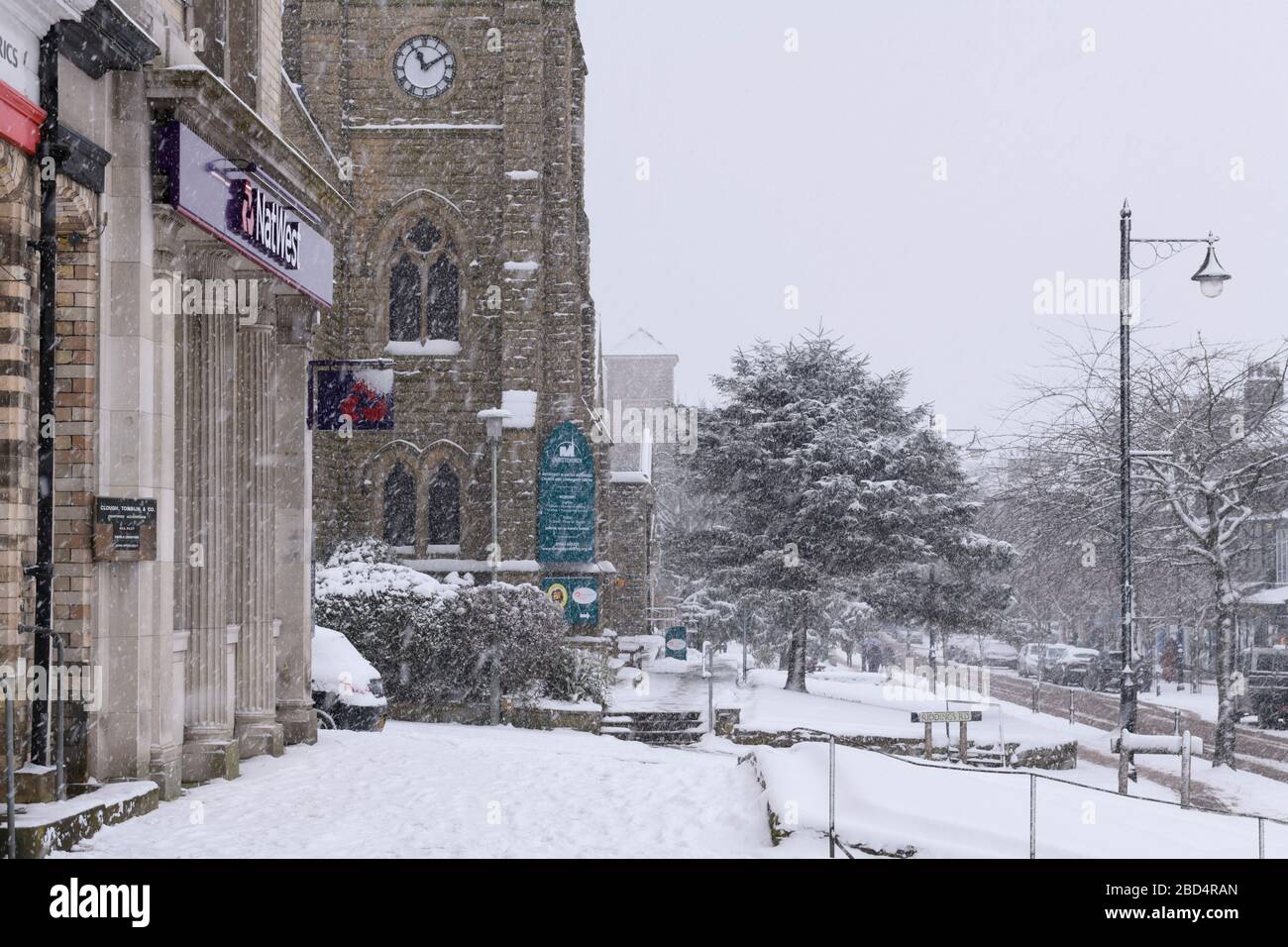 Schneebedecktes winterliches Stadtbild (schneite, schneebedeckte Hochstraße, Kirche, Geschäfte und Straße im malerischen Stadtzentrum) - The Grove, Ilkley, Yorkshire, England, Großbritannien. Stockfoto