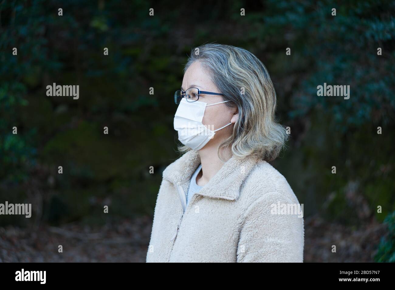 Frau 40-49 Jahre im Freien, mit Brille und weißer Maske zum Schutz vor Coronavirus COVID-19 (SARS-COV-2) und anderen ansteckenden Krankheiten. Stockfoto