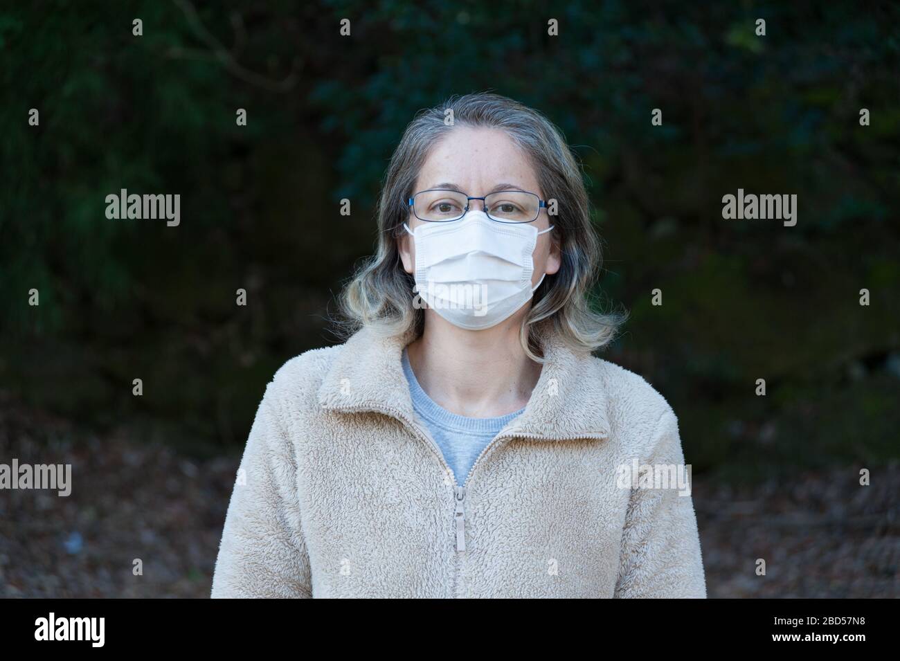Frau 40-49 Jahre im Freien, mit Brille und weißer Maske zum Schutz vor Coronavirus COVID-19 (SARS-COV-2) und anderen ansteckenden Krankheiten. Stockfoto