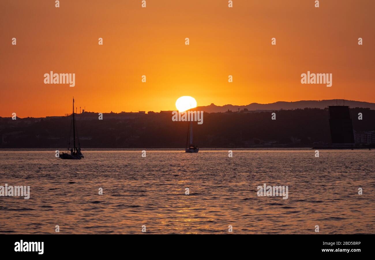 Sonnenuntergang über dem Tejo; Lissabon, Portugal. Ein ruhiger Blick auf den Sonnenuntergang mit einer Vordergrundyacht, die den Blick einzieht. Stockfoto