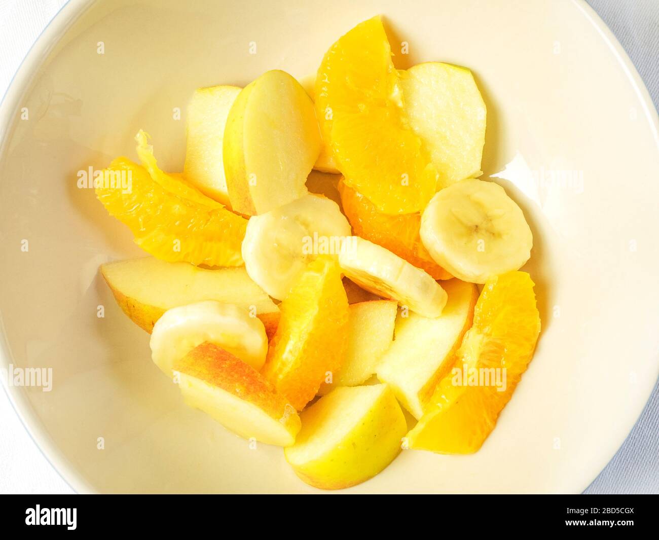 Eine Schüssel Obstsalat mit orangefarbenen Segmenten und geschnittenen Äpfeln und Bananen von oben auf einem weißen Tischtuch Stockfoto