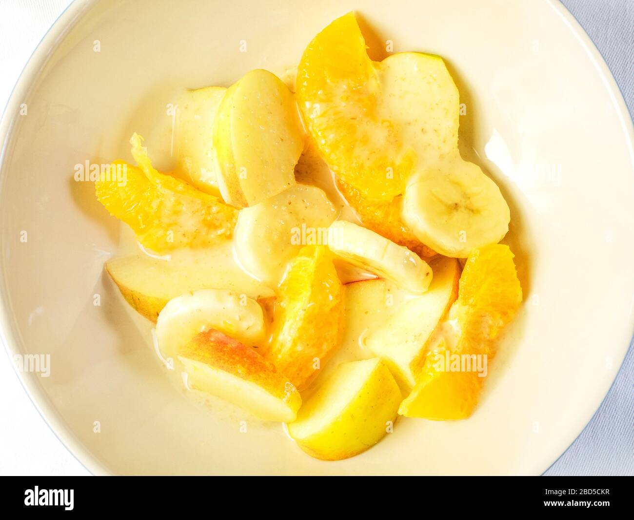 Eine Schüssel Obstsalat mit orangefarbenen Segmenten und in Scheiben geschnittenen Äpfeln und Bananen mit Hafercreme von oben auf einem weißen Tischtuch Stockfoto
