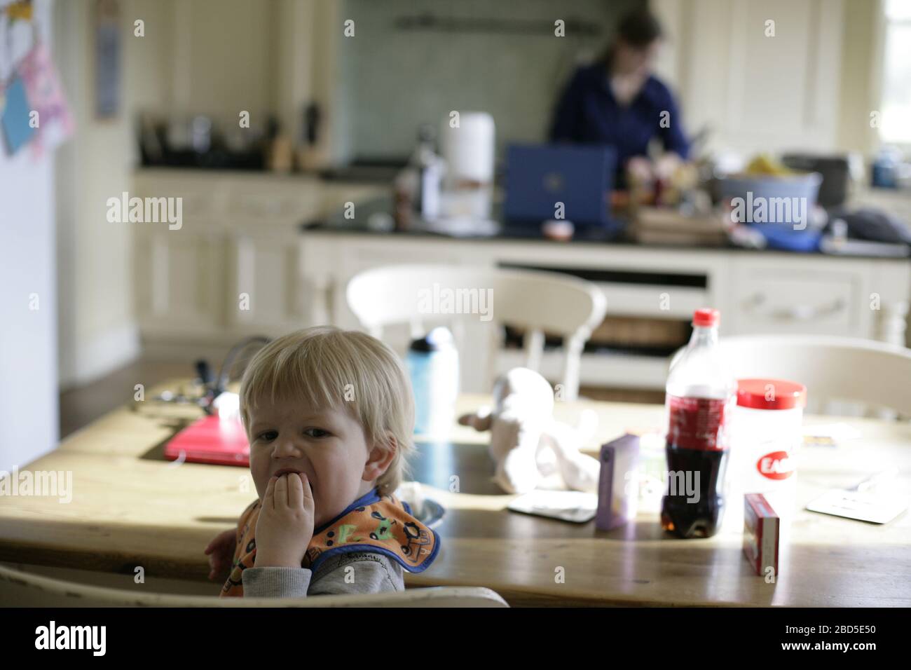 Kleinkind, das selbstgebackene Kekse isst, während Mama während der Zeit der Selbstisolierung während der COVID-19-Coronavirus-Pandemie 2020 in der Küche arbeitet Stockfoto