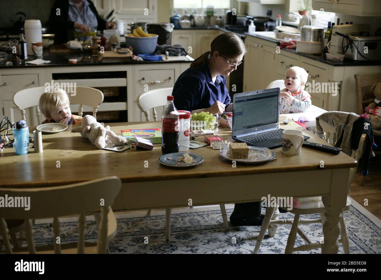 Mutter füttert ihre Kinder beim Essen am Küchentisch während der Arbeit von zu Hause während der Zeit der Selbstisolation - 2020 COVID-19 Coronavirus Pandemie Stockfoto