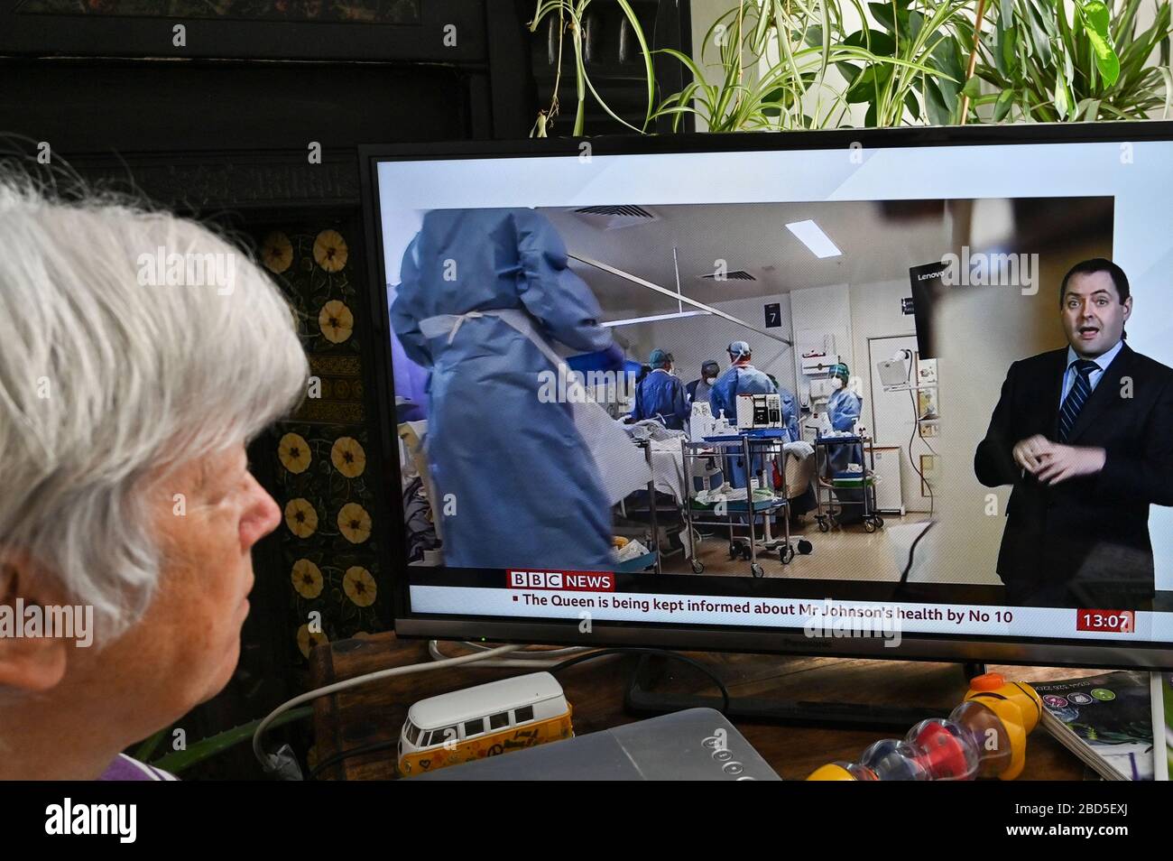 Ältere Frau, die die TV-Nachrichten mit einem Bericht über persönliche Schutzausrüstung und Pflege auf der Intensivstation verfolgt. Stockfoto