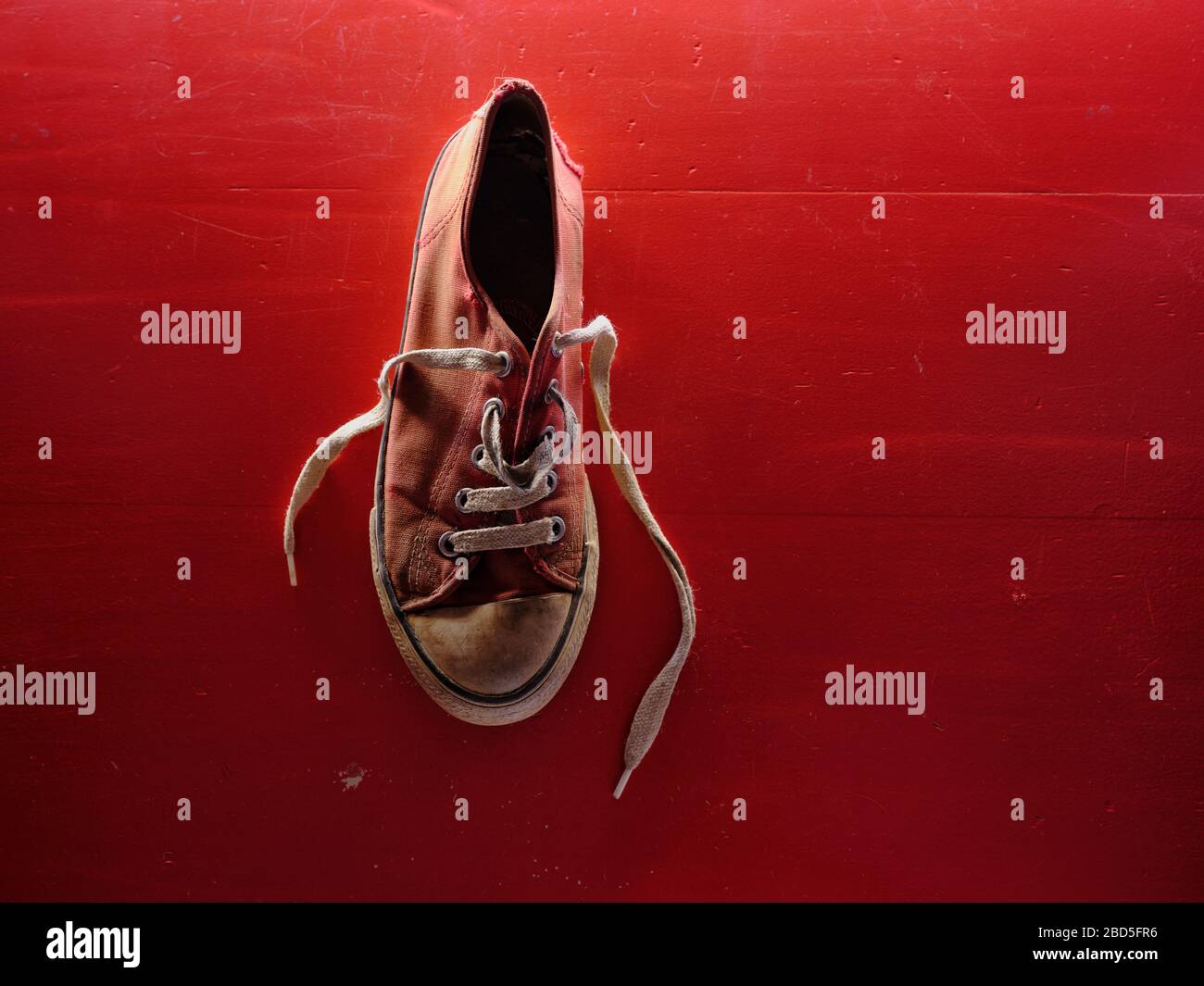 Hochauflösendes Nahaufnahme Foto eines einzigen alten und getragenen roten Sneakers auf rotem Hintergrund mit Kopierfläche. Stockfoto