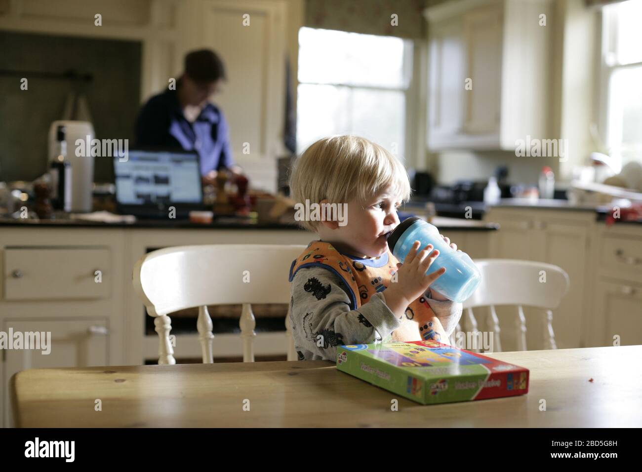 Kind Kleinkind trinken aus Dinks Flasche während Mutter Kochen Abendessen in der Küche während der Zeit der Selbstisolierung - 2020 COVID-19 Coronavirus Pandemie Stockfoto