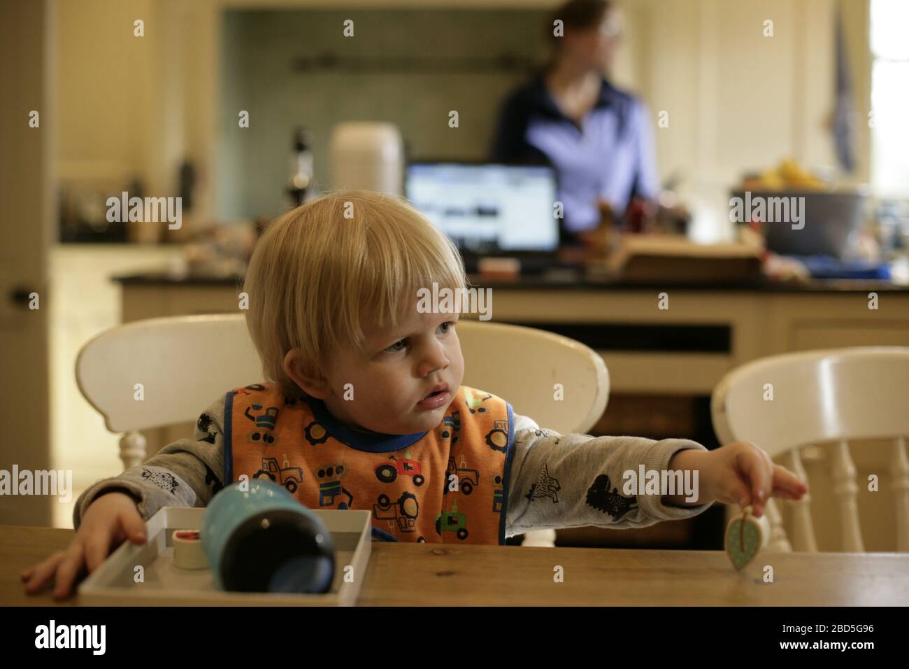 Kind Kleinkind spielen mit Puzzle, während Mutter kocht Abendessen in der Küche während der Zeit der Selbstisolation - 2020 COVID-19 Coronavirus Pandemie Stockfoto