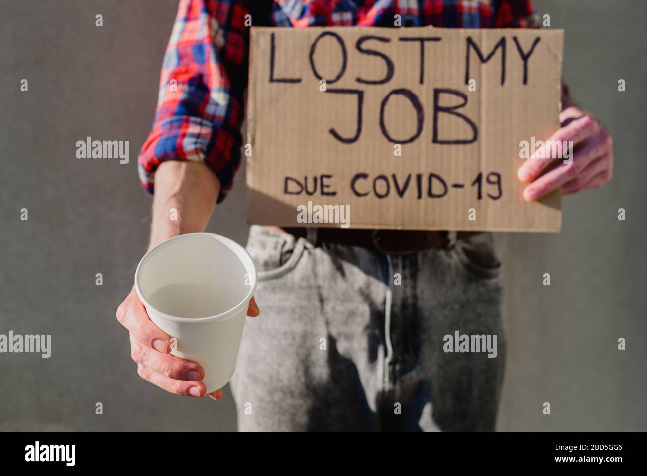Mann Arbeiter in Plaid Hemd mit Pappschild VERLOREN ARBEIT. Arbeitslos, Arbeitslosigkeit aufgrund des Kovid-19-Konzepts. Mit Papierbecher um Geld bitten Stockfoto
