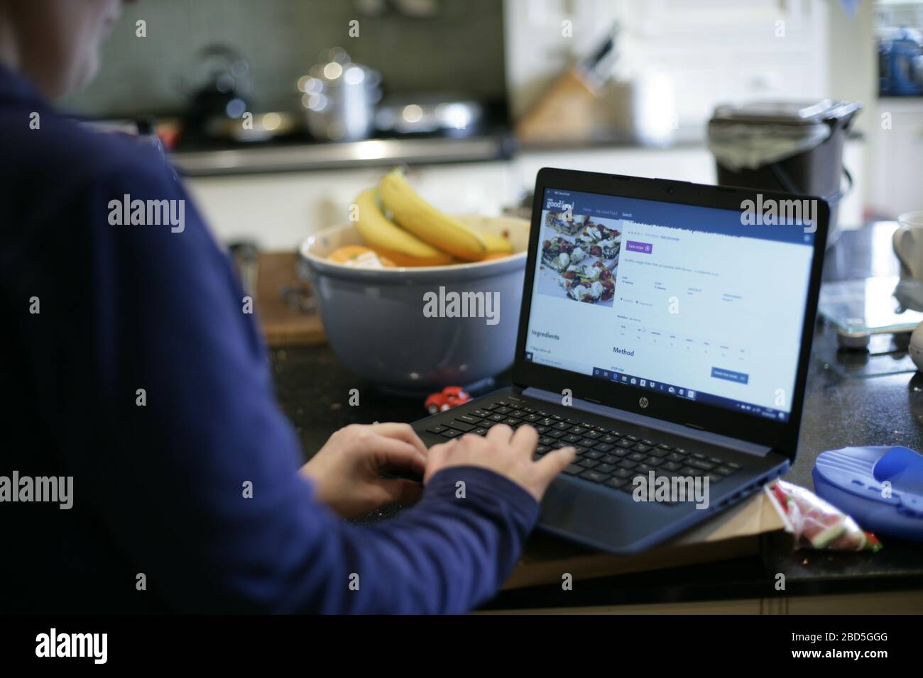 Mutter bereitet Familienessen zu Hause zu, während sie während der Selbstisolierung während der COVID-19-Pandemie 2020 in der Küche am Laptop arbeitet Stockfoto