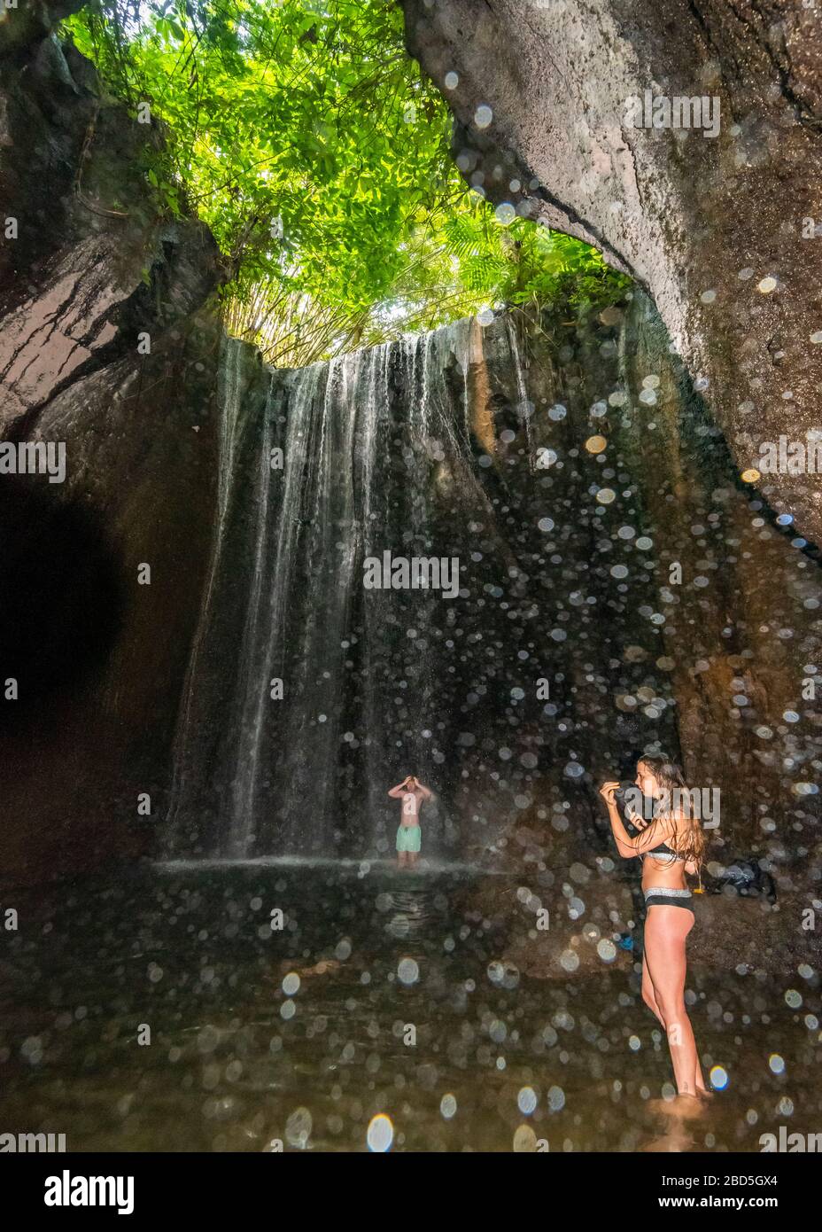 Vertikaler Blick auf Touristen, die in den Tukad Cepung-Wasserfällen in Bali, Indonesien, stehen. Stockfoto