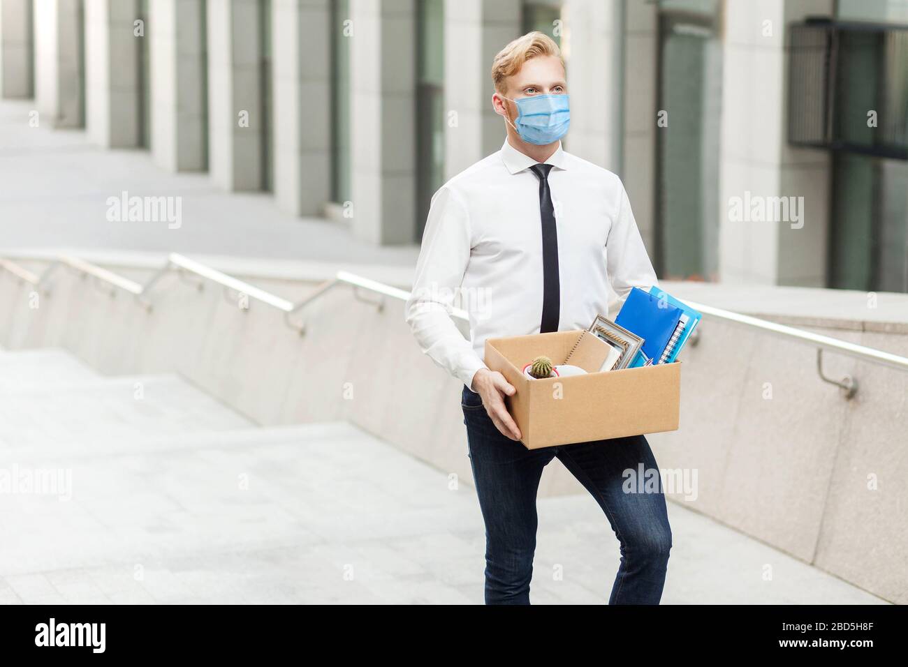 Der junge Mann in weißem Hemd mit chirurgischer medizinischer Maske hat einen neuen Job, der zu einer neuen besseren Arbeit wird. Außenaufnahmen in Treppen, Geschäftsaufzug, Arbeit und er Stockfoto