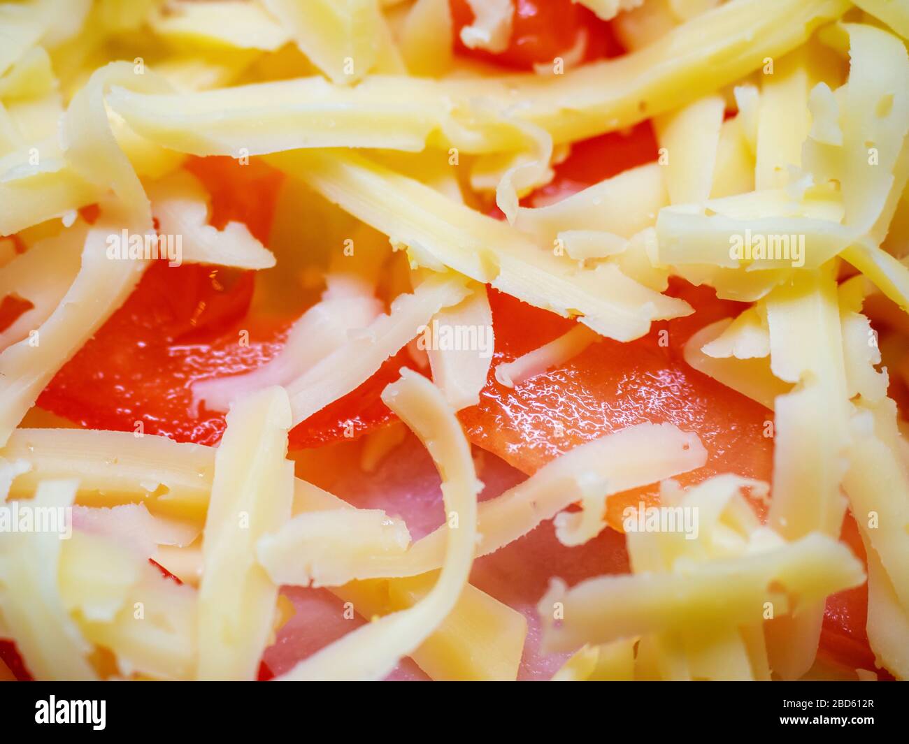 Ein Nahfoto mit Tomatenscheiben und Schinken, mit viel geriebenem Käse bestreut Stockfoto