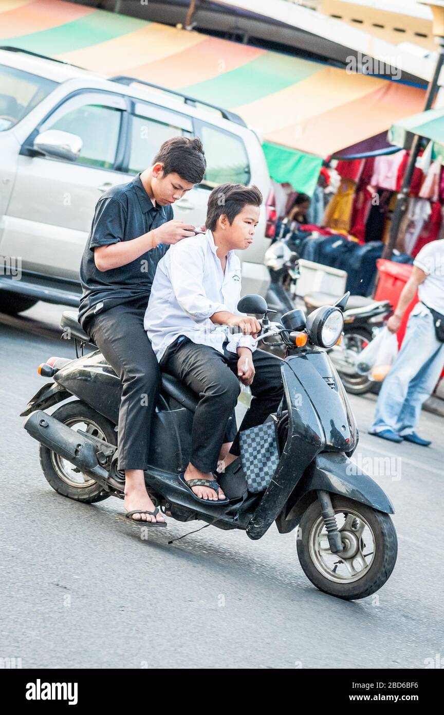 Zwei junge kambodische Studenten eilen mit dem auf sein Handy konzentrierten Passagier durch die belebten Straßen von Phnom Penh. Stockfoto