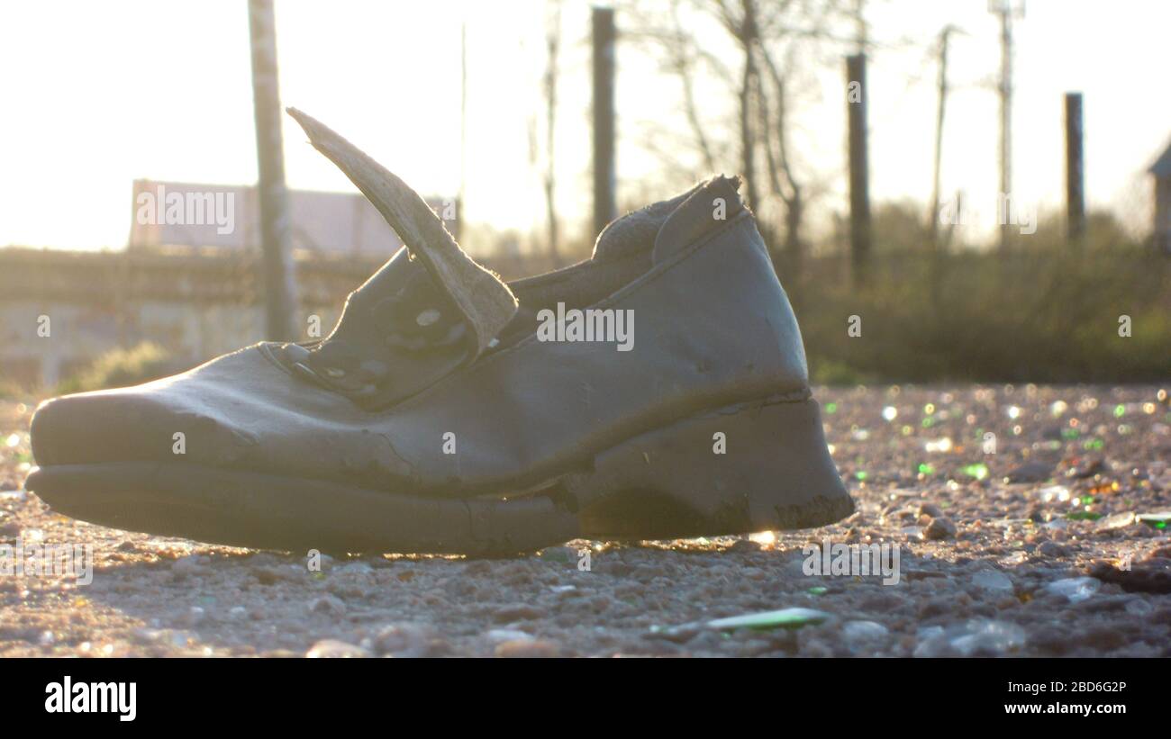 Ein alter Stiefel inmitten des städtischen Mülls liegt auf dem Bürgersteig unter den Strahlen eines sonnigen Tages. Stockfoto