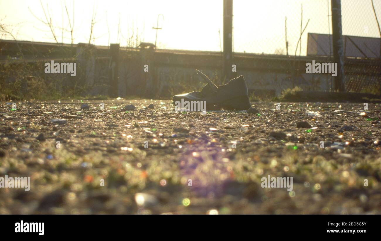 Ein alter Stiefel inmitten des städtischen Mülls liegt auf dem Bürgersteig unter den Strahlen eines sonnigen Tages. Stockfoto