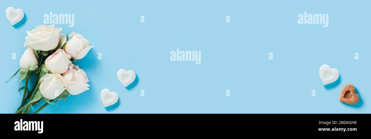 Weiße Rosen auf blauem Grund mit Zuckerstückchen in Form von Herzen. Stockfoto