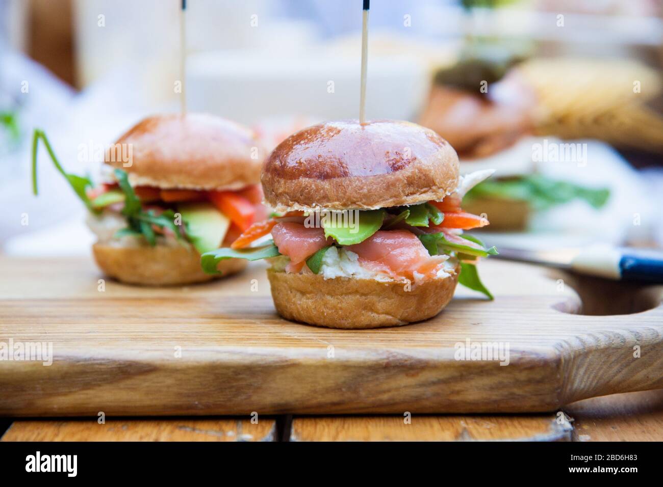 Burger mit Frischkäse, gesalzenem Lachs, Grünkohl, Avocado auf Weizenbun. Rustikaler Hintergrund. Stockfoto