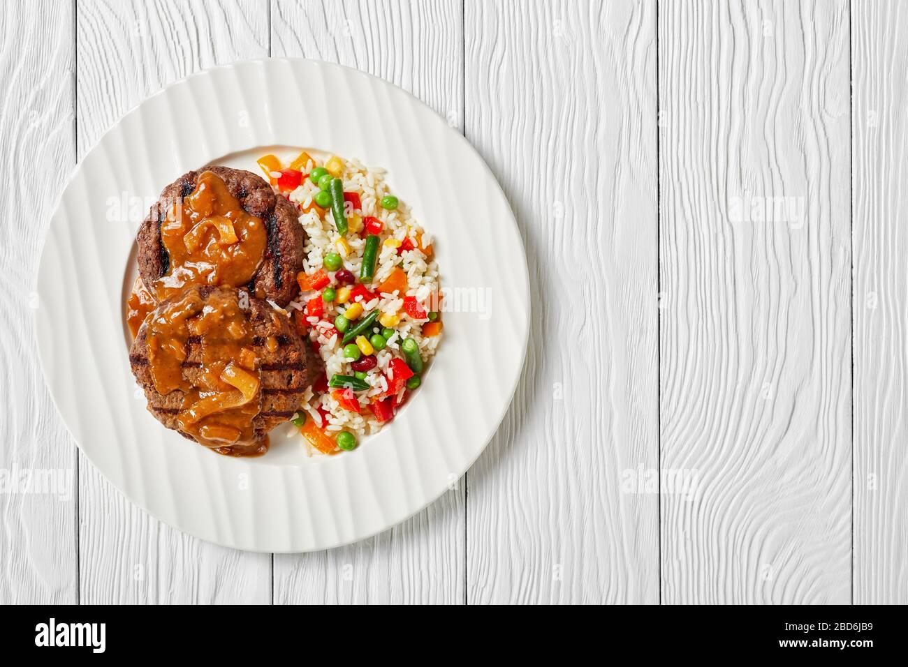 Gegrillte Hamburger mit Zwiebelgravy und Reis, gemischt mit Gemüse auf einem weißen Teller auf einem Holztisch, flacher Lay, freier Platz Stockfoto