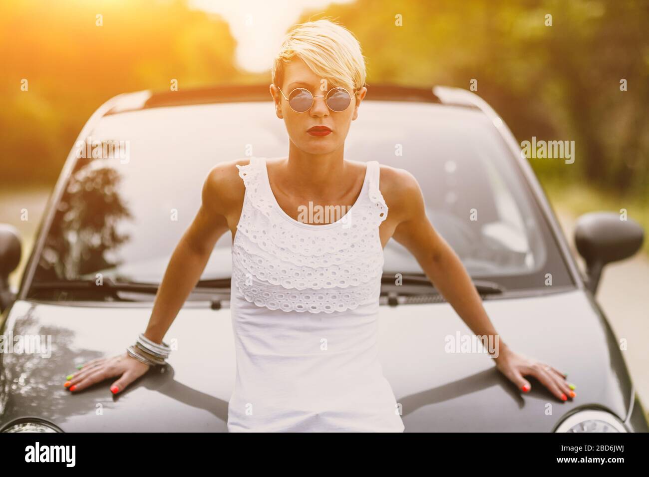 Junge hübsche modische Frau posiert auf einem Auto. Konzept junger Lifestyle. Stockfoto