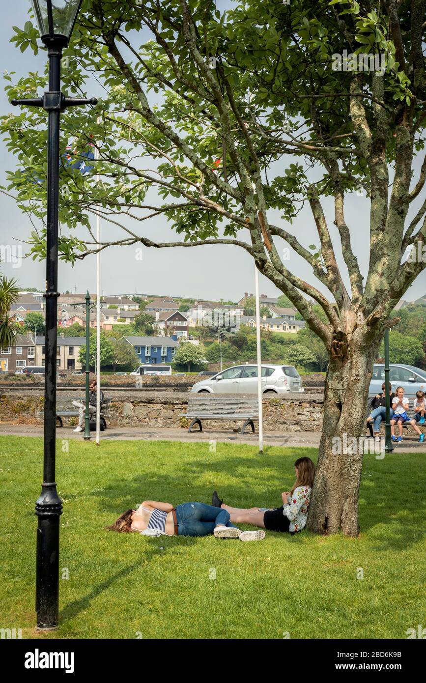 Freundinnen genießen die Sonne im Town Park in der Nähe des Hafens von Kinsale an sonnigen warmen Sommertagen in Kinsale, County Cork, Irland Stockfoto