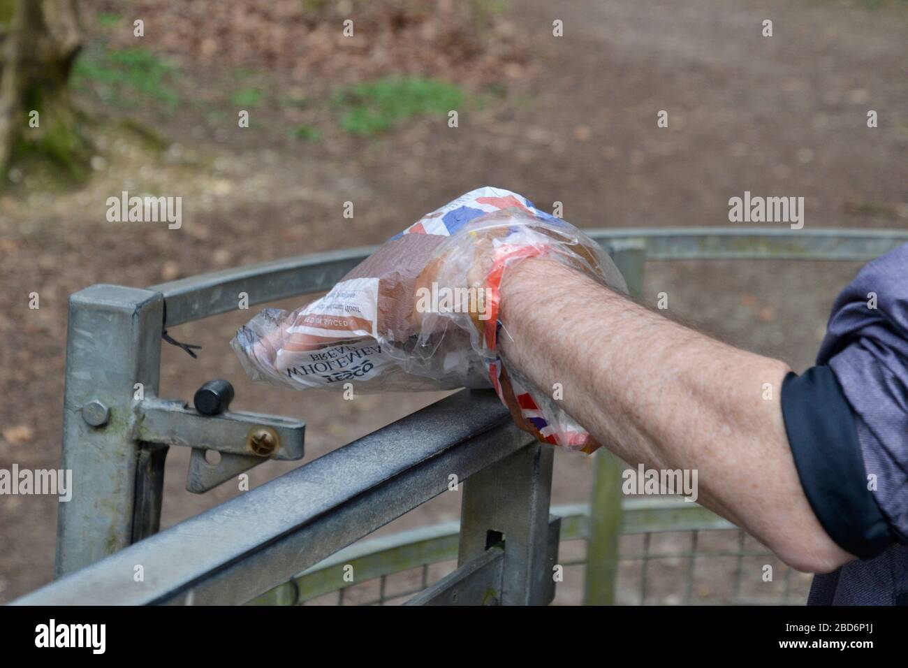 Der Mensch benutzt eine Plastiktüte, um ein Tor auf dem Land sicher zu öffnen, ohne den Riegel mit den Händen zu berühren. Coronavirus Lockdown UK Stockfoto