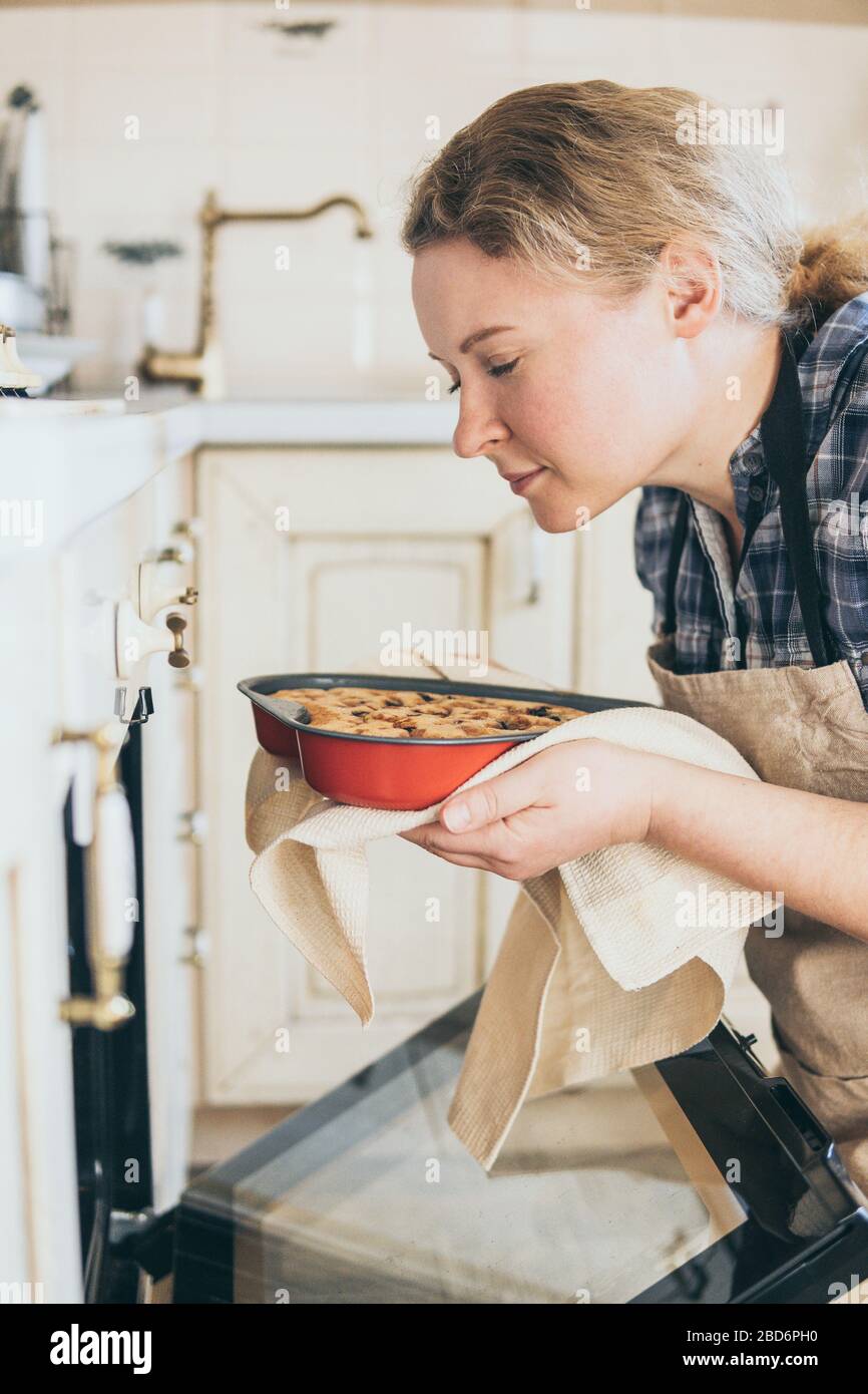 Junge blonde Frau, die herzförmige Beerenkuchen aus dem Ofen nimmt. Zu Hause kochen und mit geschlossenen Augen riechen. Stockfoto