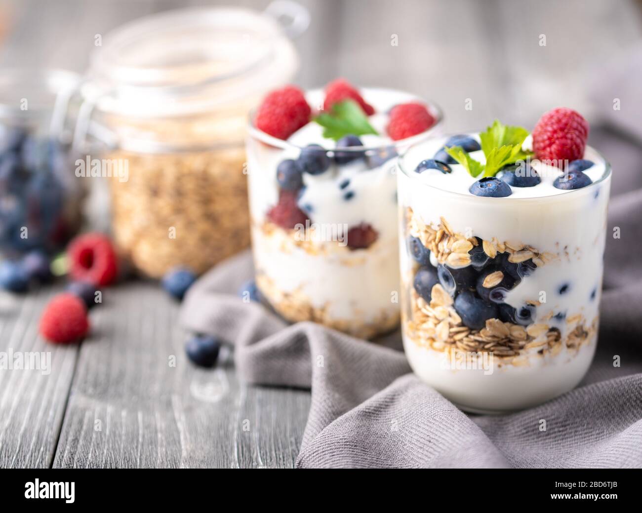 Weißer Joghurt im Glasbecher mit Himbeeren und Blaubeeren auf grauer Serviette. Stockfoto
